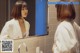 A woman in a bathrobe looking at herself in the mirror.