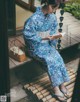 A woman in a blue and white kimono sitting on a wooden bench.